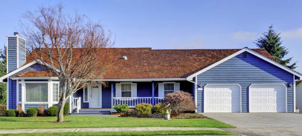 Front of a beautiful blue house with a brown roof and white garage doors