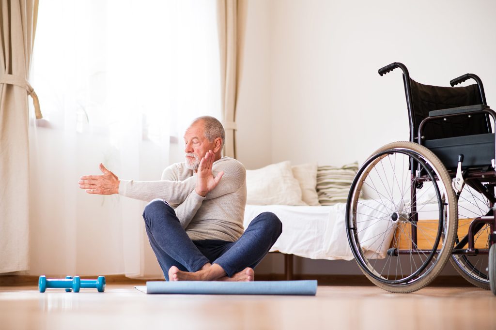 Active senior man doing exercise at home with a wheelchair next to him