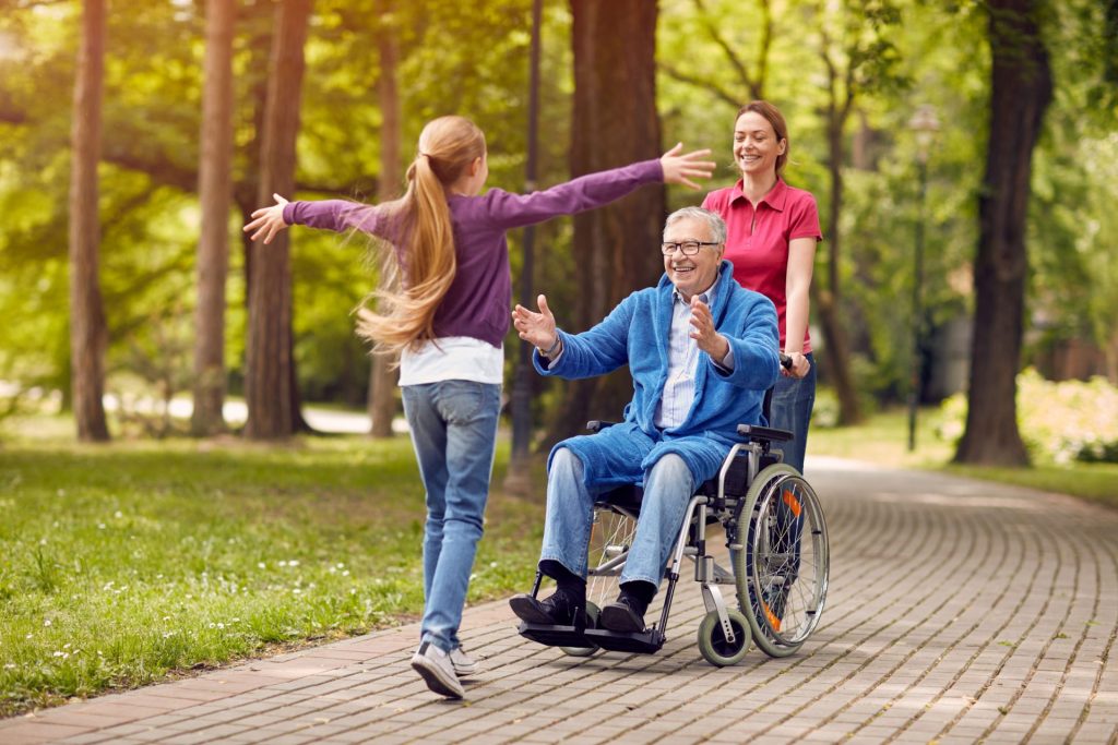 An elderly gentleman in a wheelchair outdoors with his family