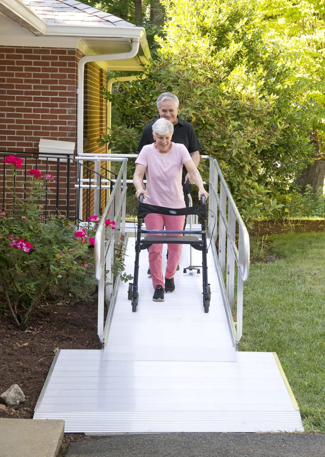 Elderly woman walking down a ramp with a walking aid and assistance from a gentleman