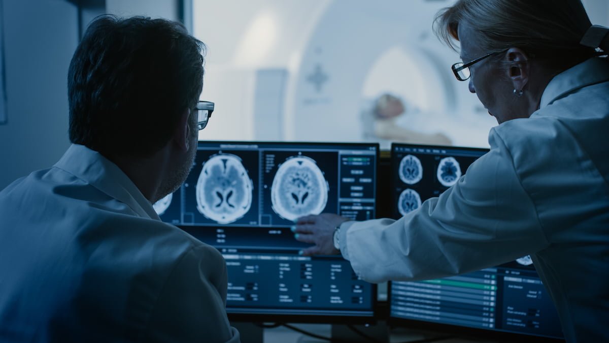 A Doctor and Radiologist Discussing Diagnosis while Watching the Procedure and Monitors Showing Brain Scans Result.